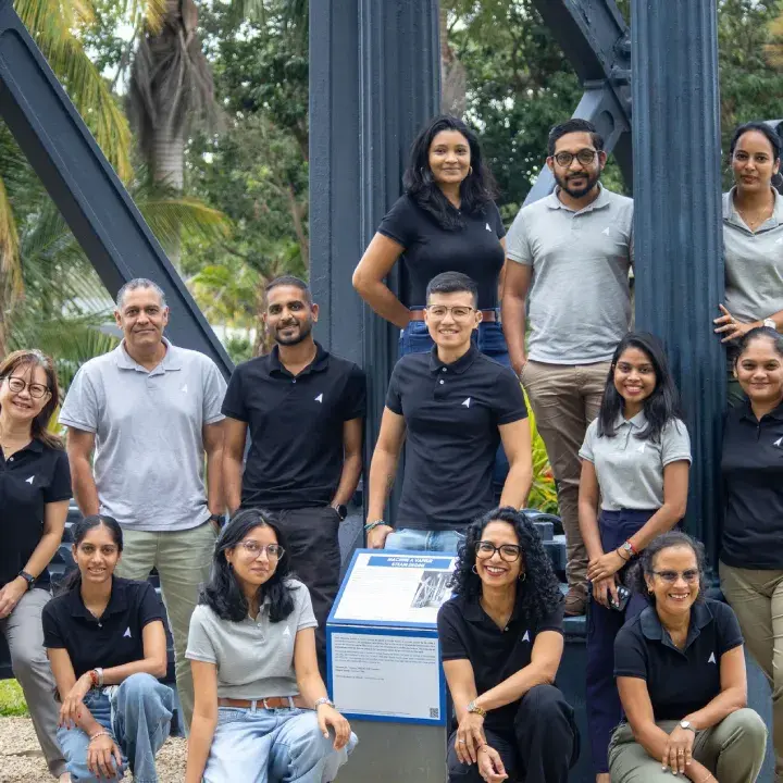 Novaterra finance and administration team in black and grey polos posing by a steel heritage structure at Beau Plan