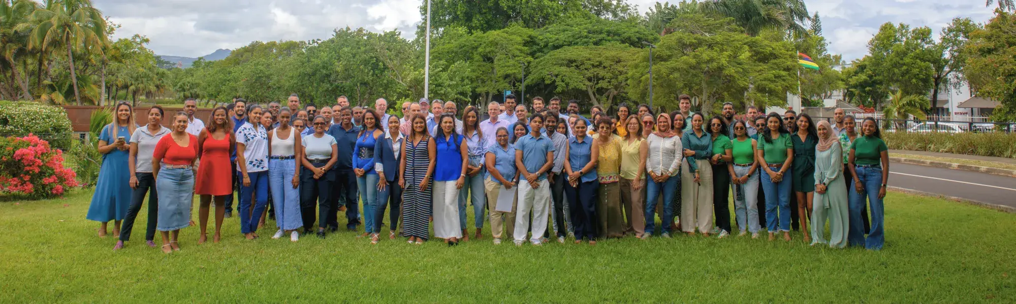 The Novaterra team, about a hundred staff, posing together on a lawn lined with trees and a Mauritian flag in the north of Mauritius