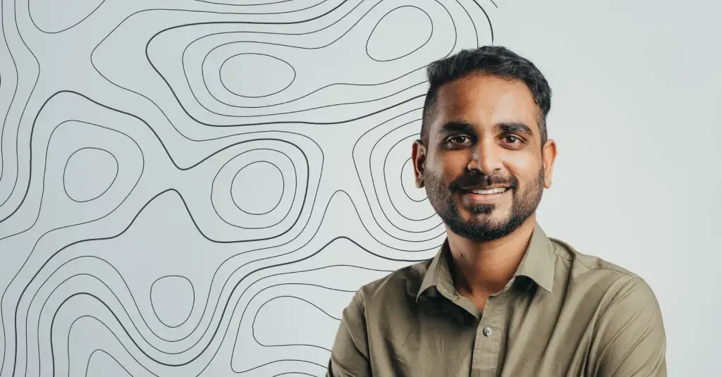 Yash, Accounts Receivable Clerk in Novaterra's Finance Department, smiling in an olive shirt before a contour-line wall