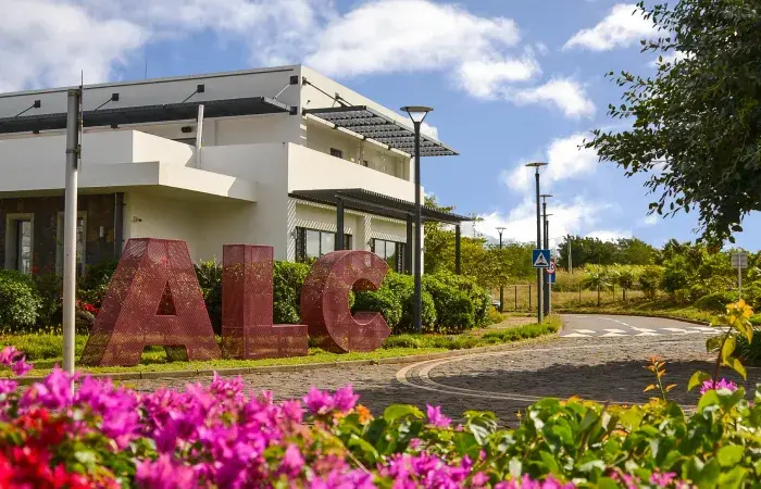 Large red ALC letters in front of the white African Leadership College campus at Beau Plan, with pink bougainvillea