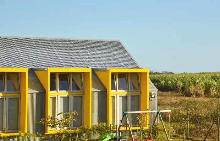 Greencoast International School at Mon Rocher, a corrugated metal building with yellow window frames beside sugarcane fields
