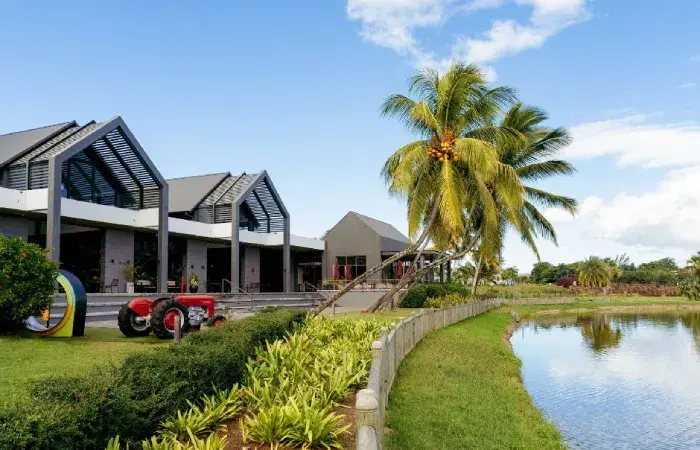 Mahogany Shopping Promenade at Beau Plan with gabled buildings, a red vintage tractor, palm trees and a pond