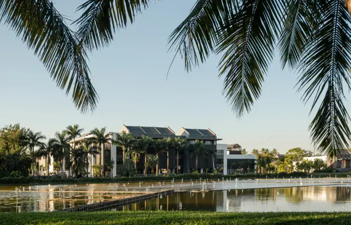 Modern residential buildings among palm trees beside a lake with fountains at Beau Plan Smart City, framed by palm fronds