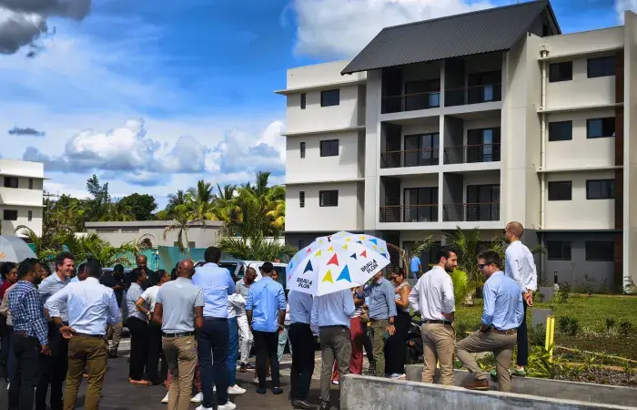 Crowd gathered outside a new Indigo Phase 1 apartment building at Beau Plan, one holding a Beau Plan umbrella, at its delivery