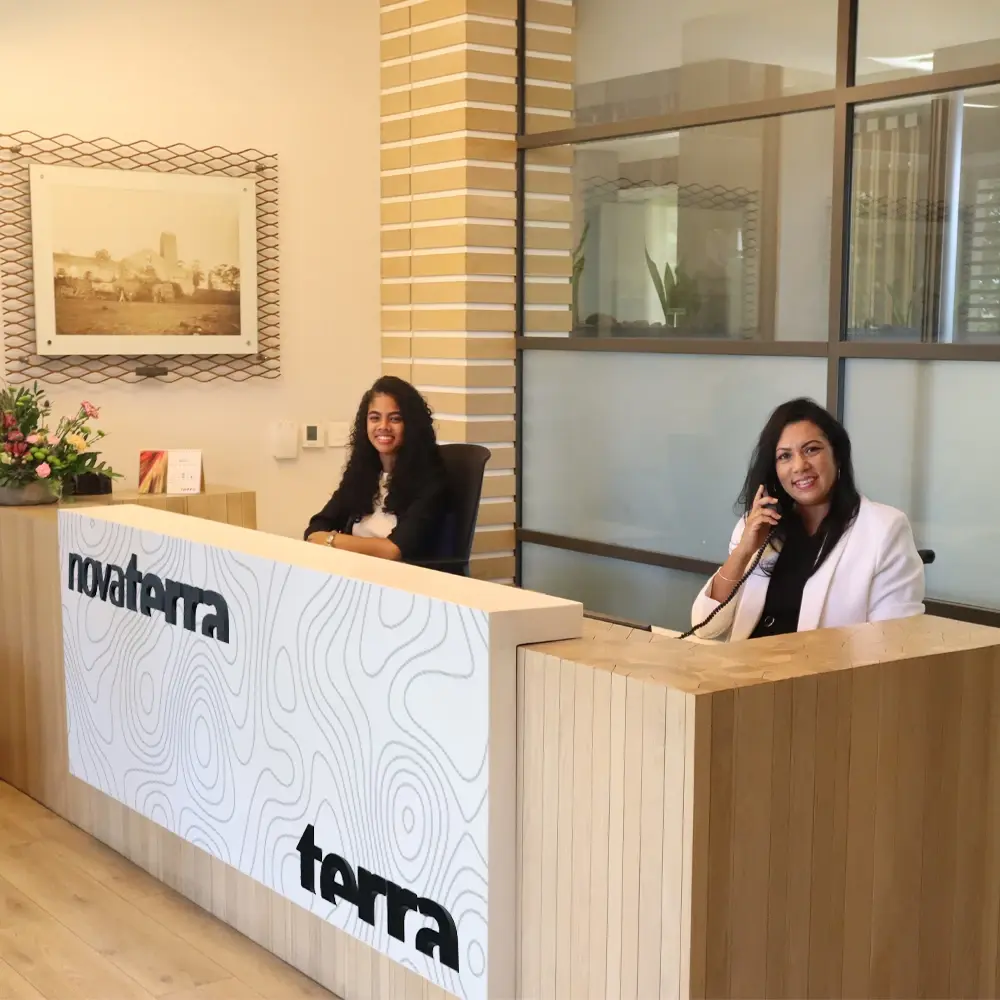 Two smiling receptionists, one on the phone, at the Novaterra and Terra branded front desk in the Beau Plan Business Park office