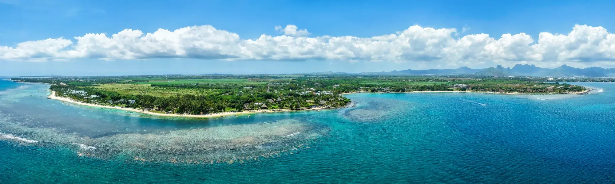 Aerial panorama of the Balaclava coast in Mauritius, with turquoise lagoon, coral reef, green land and distant mountains