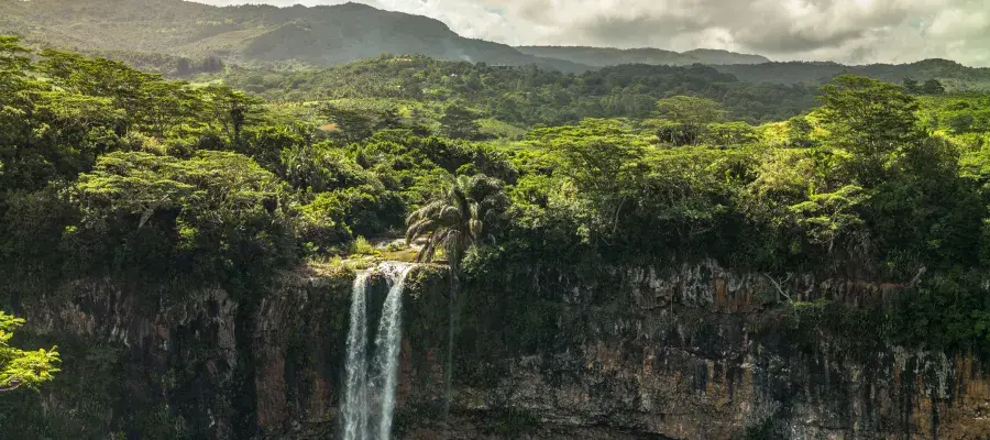 Waterfall plunging over a basalt cliff amid dense tropical forest and green hills in Mauritius