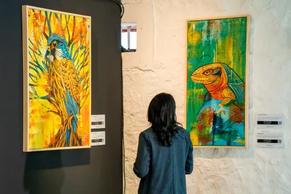 Visiteuse devant deux peintures colorées d’un oiseau et d’un lézard exposées au Creative Park de Beau Plan