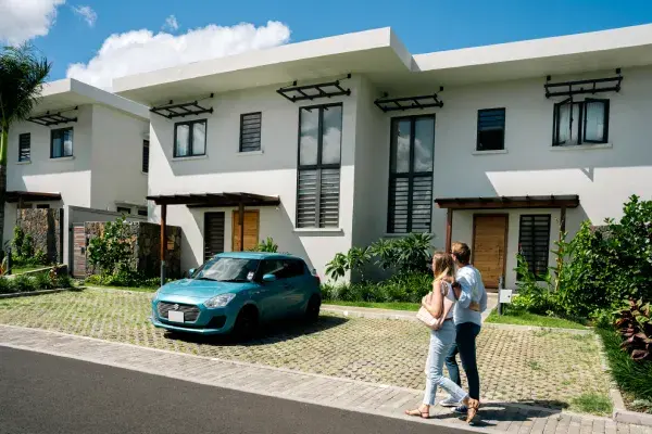Couple se promenant devant des maisons blanches à étage d'un quartier résidentiel de Beau Plan, voiture bleue garée