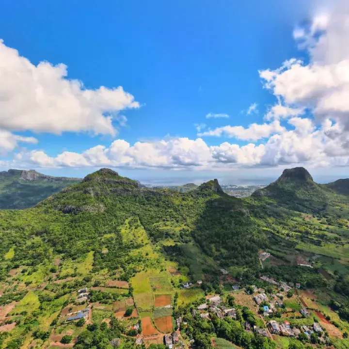 Aerial view of green mountain peaks and farmland around Domaine de Crève-Cœur under a blue sky with white clouds