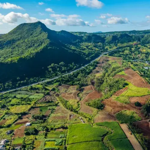Aerial drone view of Domaine de Crève-Cœur farmland plots below a green mountain, with a highway crossing the valley