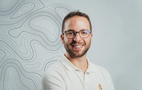 Fabrice Noel, Novaterra Sales and Leasing Executive, smiling in a white polo shirt before a contour-line wall