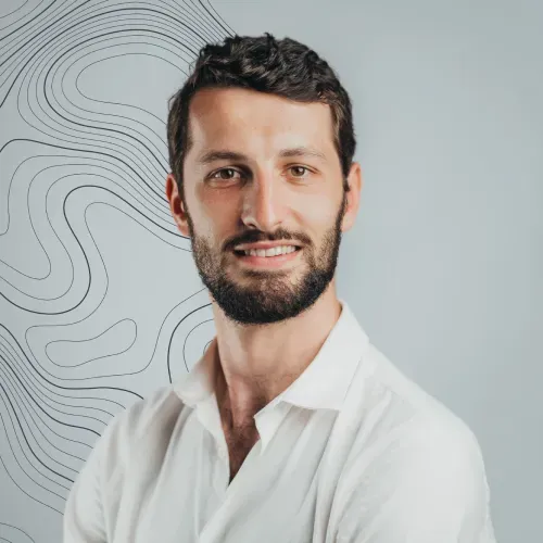 Romain Espitalier Noel, Novaterra Sales and Leasing Executive, smiling in a white shirt against a grey contour-line backdrop