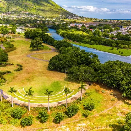 Vue aérienne de Cap Tamarin Smart City : parc avec amphithéâtre en gradins, palmiers, rivière et montagne en arrière-plan