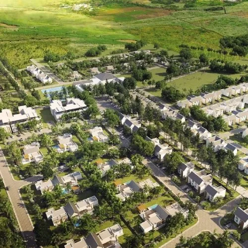 Vue aérienne de Mon Trésor Smart City avec villas, piscines, rangées de maisons et palmiers entourés de champs verts