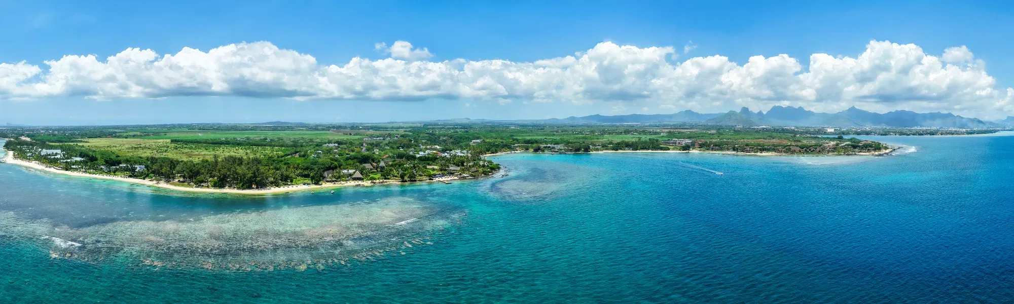 Vue aérienne panoramique de la côte mauricienne, lagon turquoise, récif corallien, terres verdoyantes et montagnes au loin