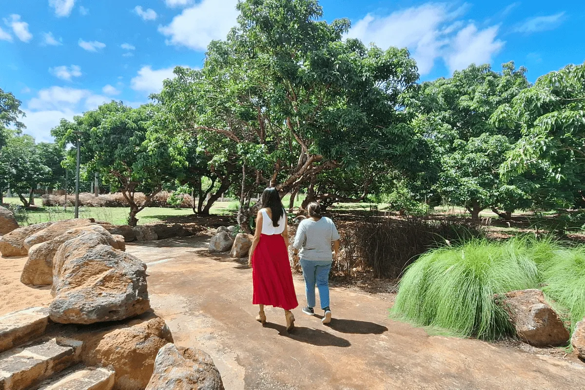 Deux femmes se promènent sur une allée bordée de rochers et de manguiers dans le parc urbain de Beau Plan