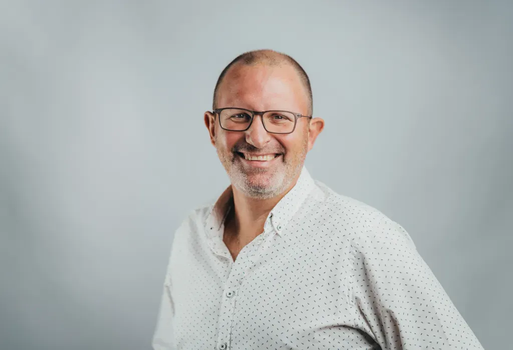 Hubert Koenig, Novaterra Senior Development Manager, smiling in glasses and a white patterned shirt against a grey backdrop