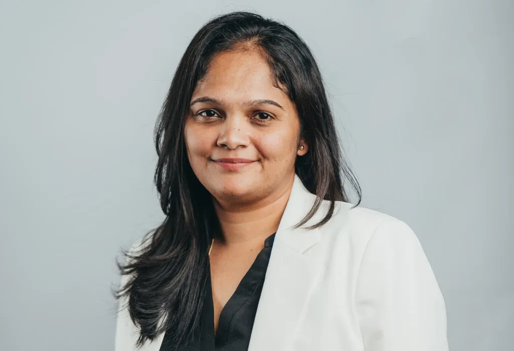 Portrait of Christel Theodore, Senior Accountant at Novaterra, smiling in a white blazer against a grey backdrop