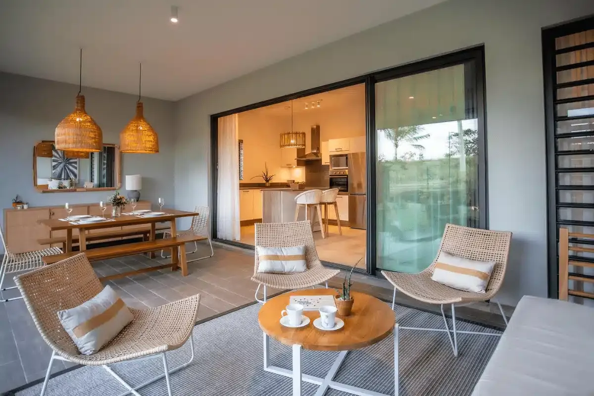Furnished terrace with wicker chairs and dining table opening onto a fitted kitchen, showing a new home with a Déco Pack