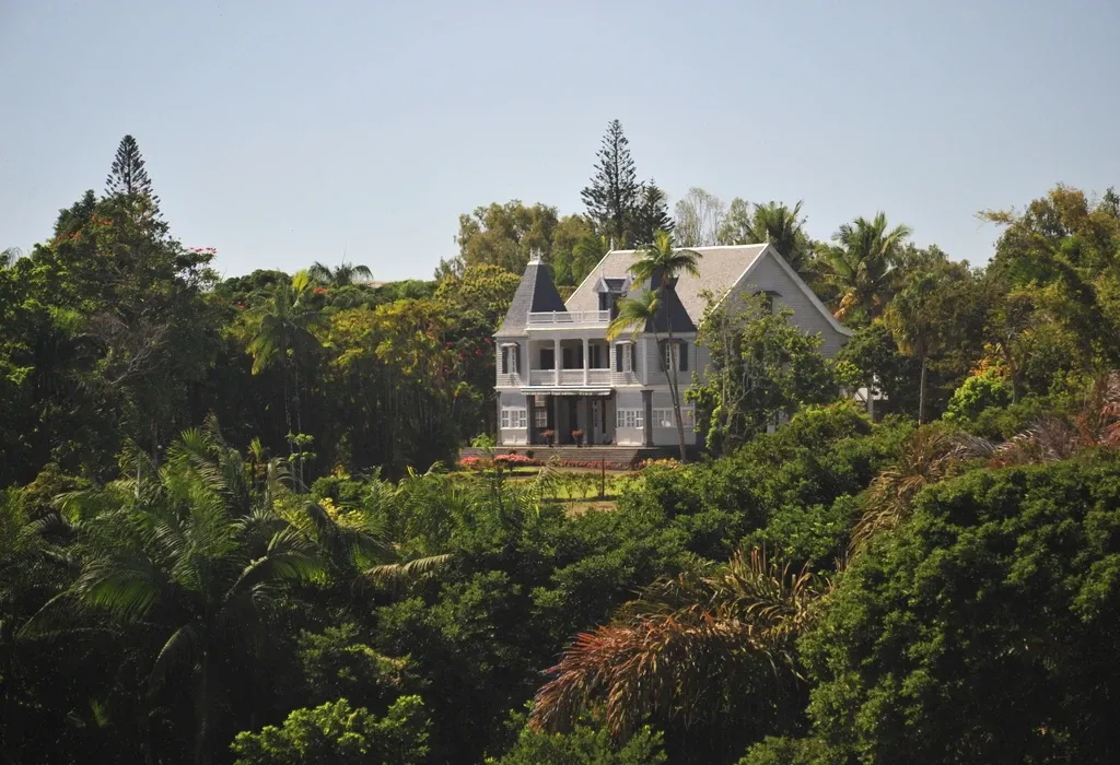 Grey colonial-style two-storey house with verandas and turrets, set among lush tropical trees and palms in Mauritius