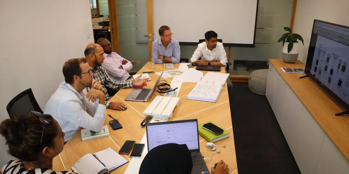 Beau Plan design review committee members around a meeting table reviewing architectural plans shown on a wall screen