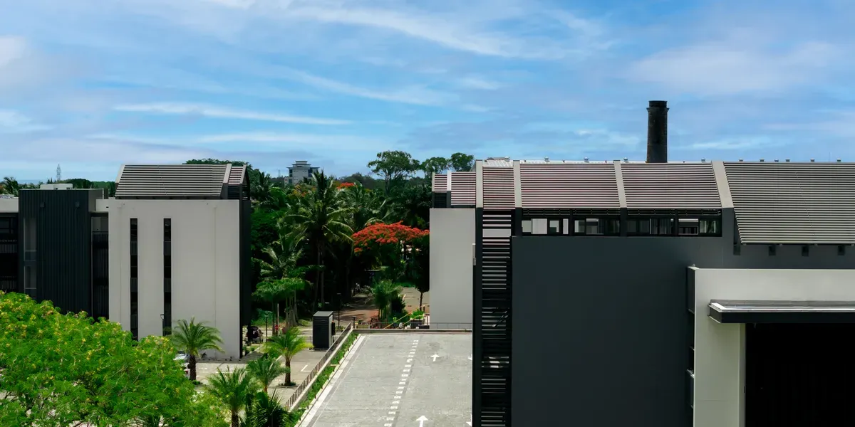 Modern white and black buildings with sloped roofs and a sugar mill chimney among tropical trees in Beau Plan