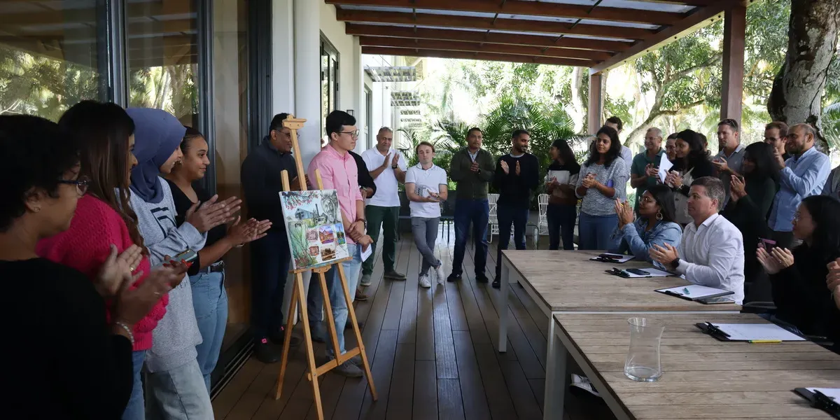 Novaterra team members applauding on a covered terrace around an easel displaying a colourful poster, beside meeting tables