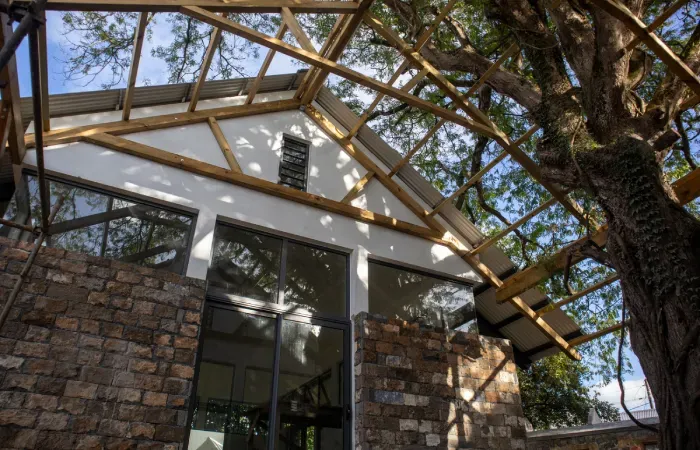 HEI Schools Mauritius building in Forbach, old stone walls with large glazed windows under a timber pergola beside a tree