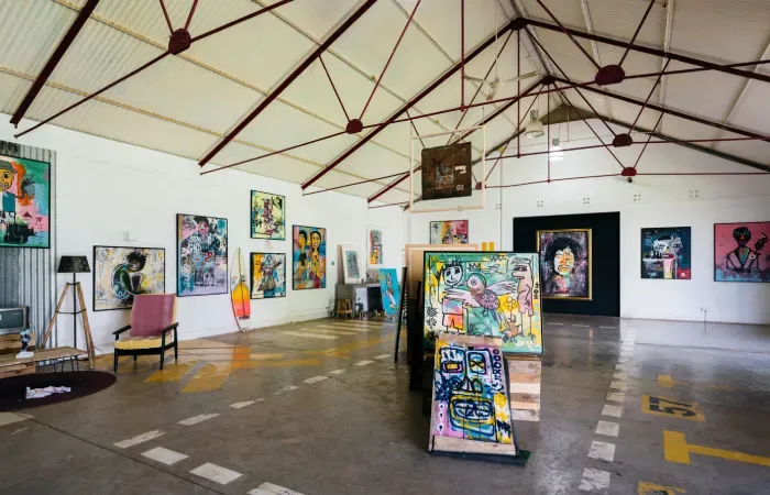 Former warehouse at Beau Plan's Creative Park turned gallery, with colorful paintings on white walls under a steel-truss roof