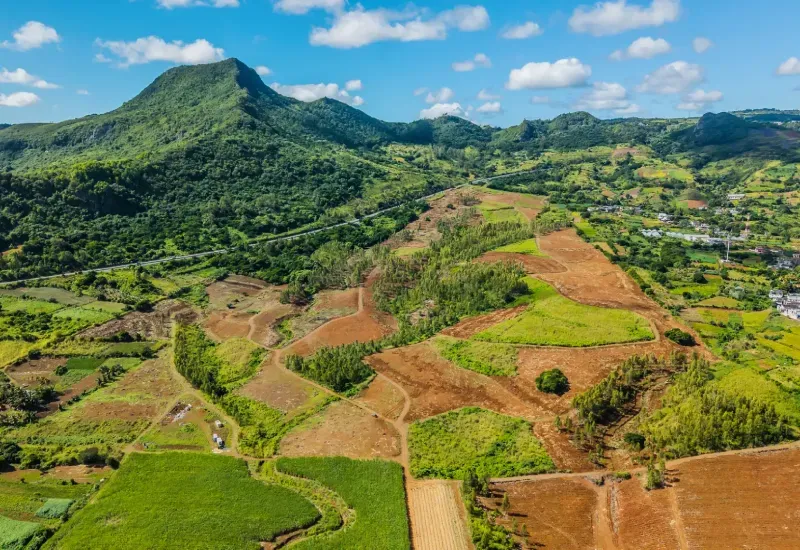 Aerial view of Domaine de Crève-Cœur agricultural plots, red earth and green fields below a lush mountain in Mauritius