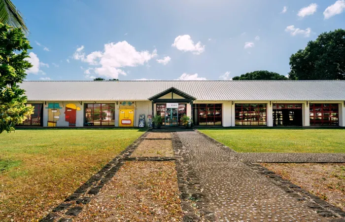 Creative Park at Beau Plan, a restored long warehouse with artist-painted colorful faces, red-framed windows and a stone path