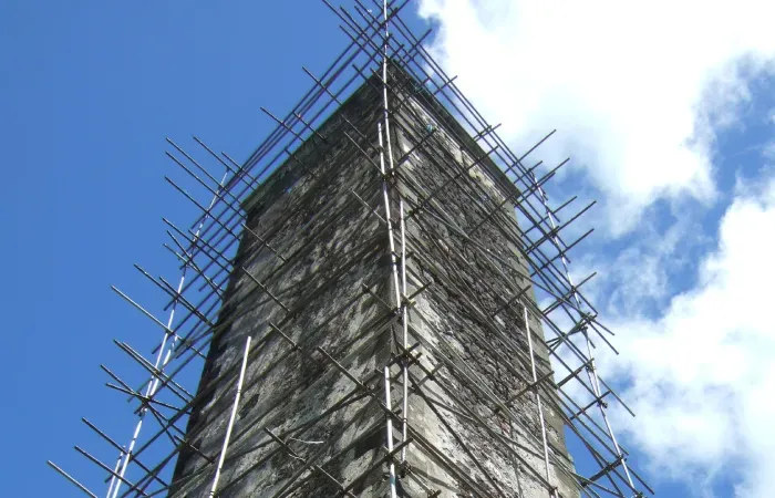 Historic stone chimney of Mon Rocher wrapped in restoration scaffolding against a blue sky
