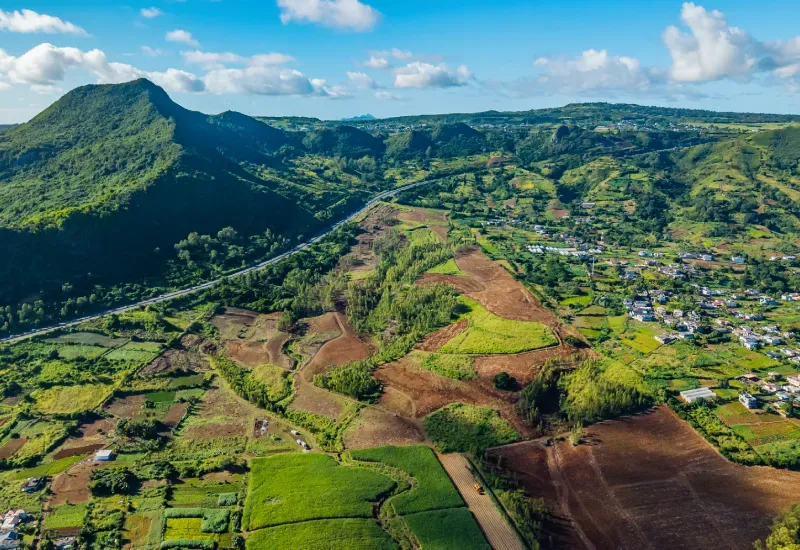 Aerial view of Domaine de Crève-Cœur farmland in a green valley beside a mountain, a highway and a village