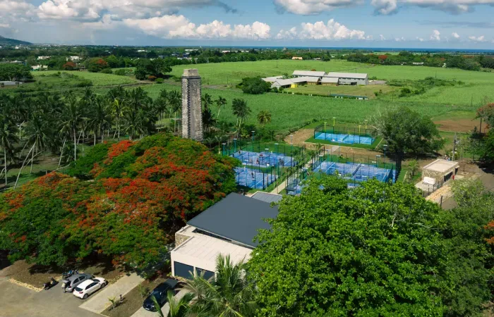 Aerial view of Mon Rocher with its historic stone chimney, flowering flame trees and blue padel courts amid cane fields