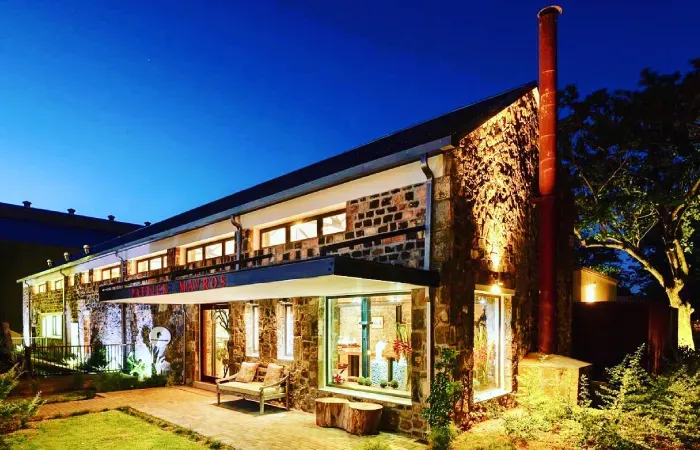 Patrick Mavros jewellery store in a restored stone former foundry at Beau Plan, lit up at dusk with a tall red chimney
