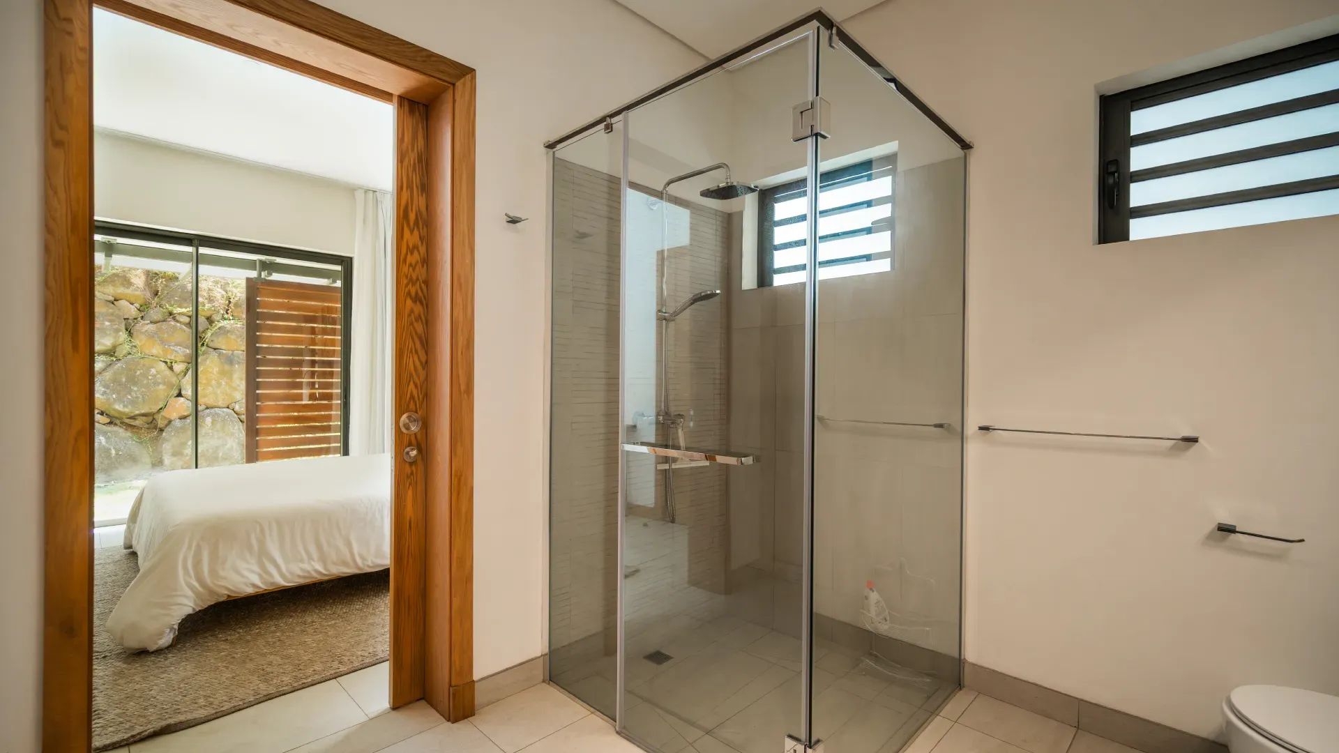 Bathroom with glass walk-in shower opening onto a bedroom in a 3-bedroom Mango Village apartment at Beau Plan