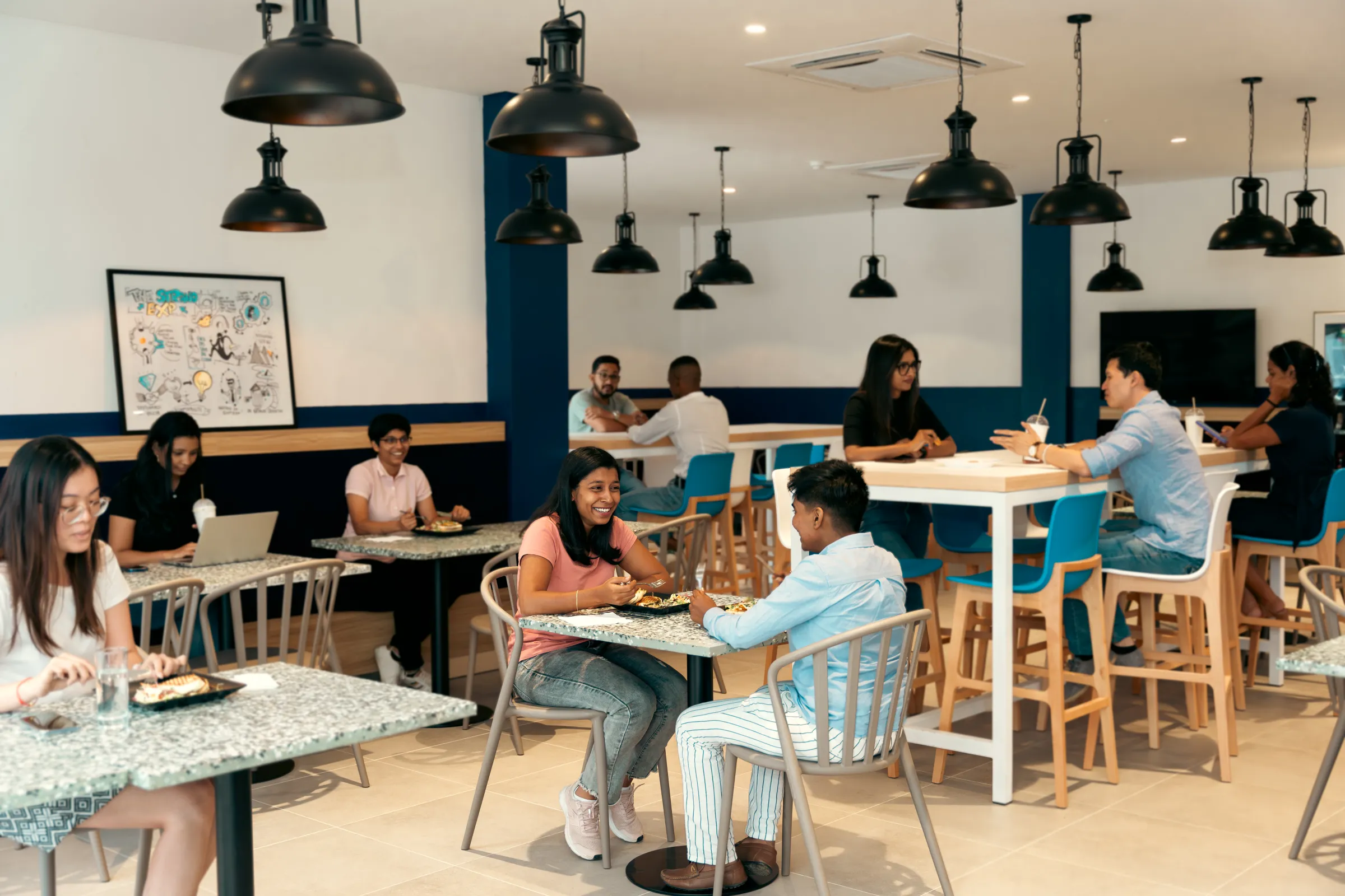 Staff eating lunch at terrazzo tables and high bar seating in the cafeteria of an office at The Strand, Beau Plan