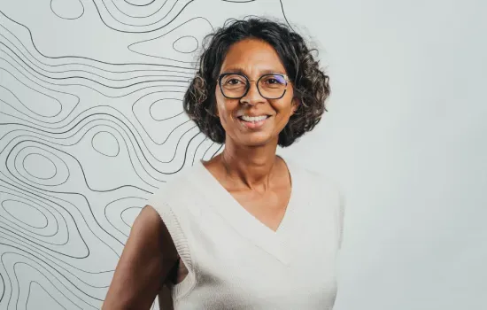 Portrait of Sarah Ah Hong, Centre & Office Manager, smiling in glasses before a wall with topographic line art
