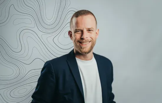 Emeric Vigier de Latour, Senior Manager Communication & Marketing, smiling in a navy blazer before a contour-line backdrop