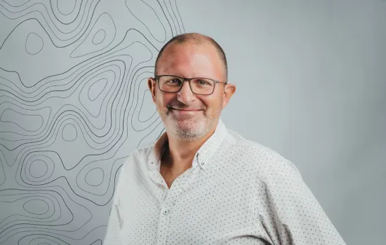 Hubert Koenig, Senior Development Manager at Novaterra, smiling in glasses and a white shirt before a contour-line wall