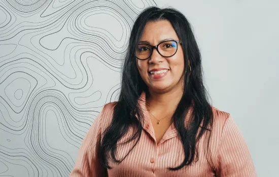Linda Gogi, Novaterra Receptionist and Administrative Assistant, smiling in glasses before a topographic line wall