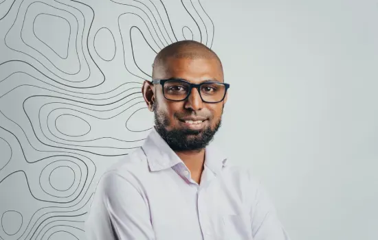 Damien Emmanuel, Architectural Technologist, smiling in glasses and a white shirt before a contour-line wall