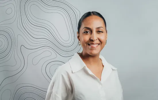Portrait of Astride Luxe, Employee Experience Officer, smiling in a white shirt before a contour-line map wall