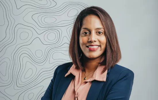 Portrait of Ashweena Poorunsing, Portfolio Lead, smiling in a navy blazer before a wall with contour line pattern