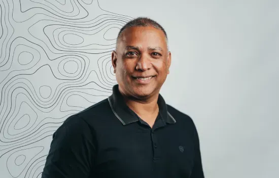 Portrait of Vikash Lingiah, Novaterra draughtsman, smiling in a black polo shirt before a topographic line pattern