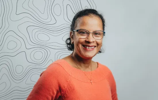 Loretta Valapinee, Novaterra Accounts & Treasury Officer, smiling in an orange sweater before a contour-line wall