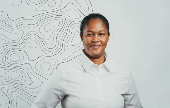 Natasha Verte, Office Attendant at Novaterra, smiling in a white shirt before a wall with topographic contour lines