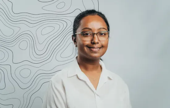 Ashwanee Mohit, Accounts Payable Officer at Novaterra, smiling in glasses and a white shirt before a contour-line wall