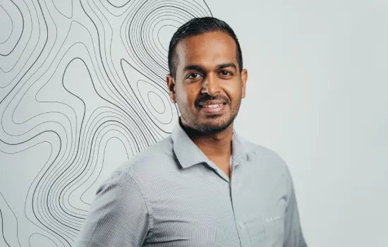 Aman Bundhun, Manager of Projects & Implementation at Novaterra, smiling in a grey shirt before a contour-line wall